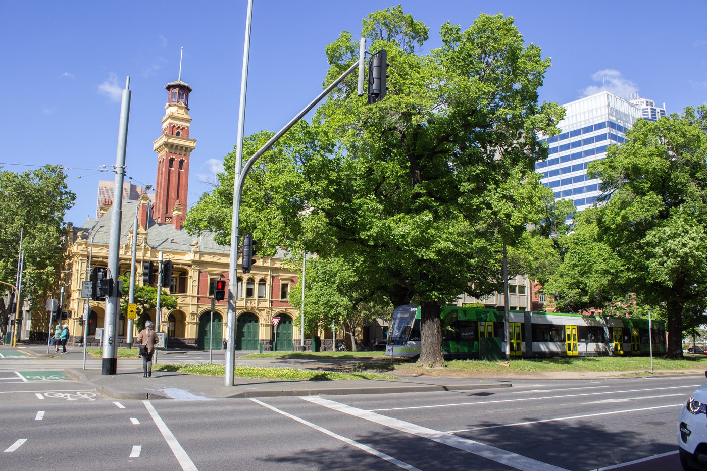 The Eastern Hill fire station tower rising above the trees on Victoria Parade, with a tram passing